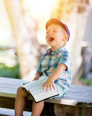 Foto von einem lachenden Jungen mit einem Buch auf dem Schoß