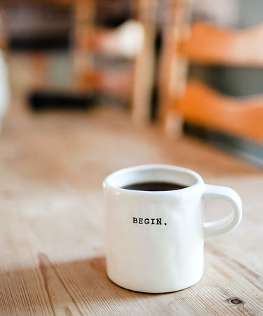 Weiße Kaffeetasse mit Schriftzug "Begin" auf einem Tisch