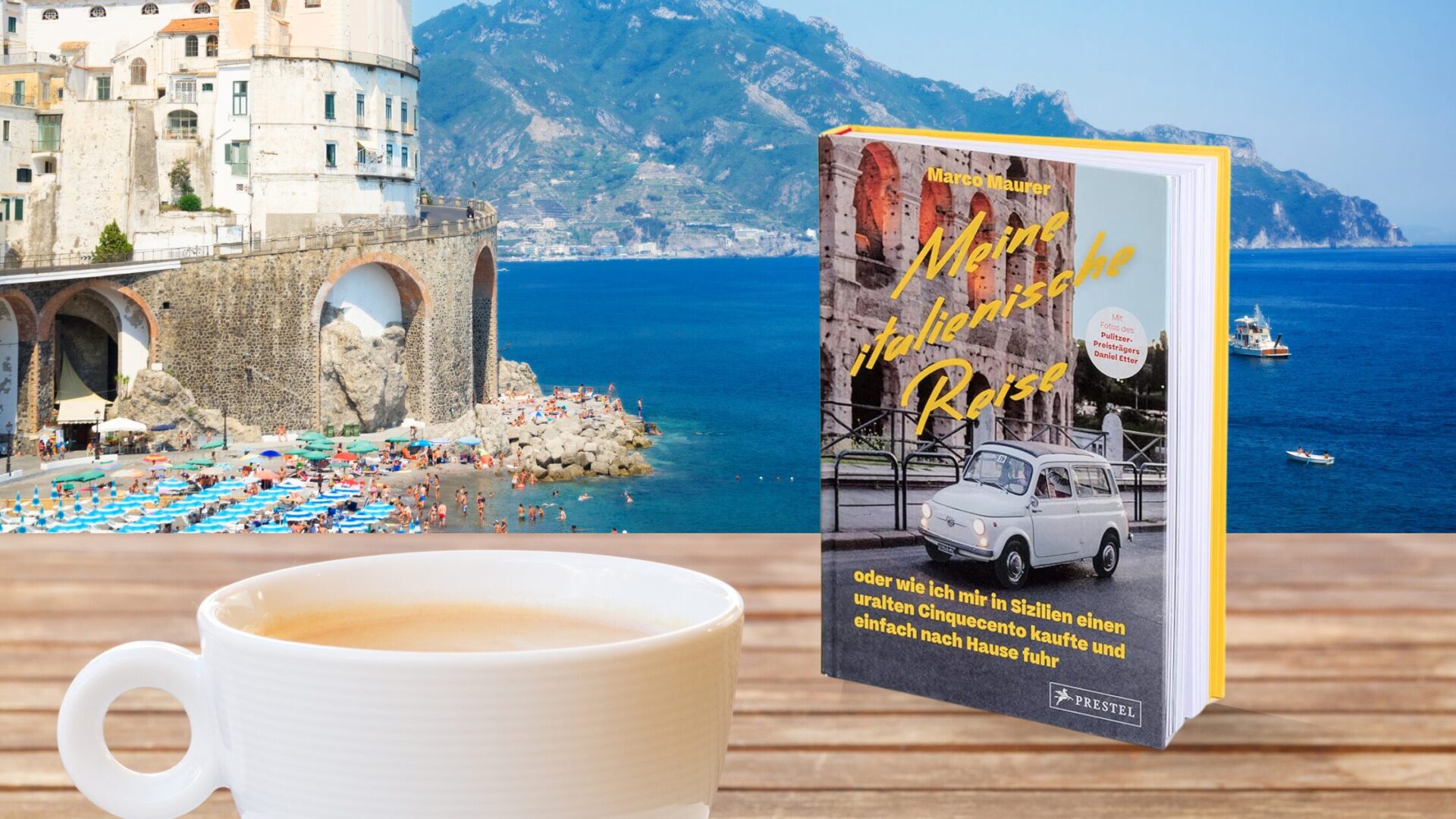 Beitragsbild zur Buchrezension "Meine italienische Reise". Foto der italienischen Küste mit einem Tisch, auf dem das Buch und eine Kaffeetasse stehen.